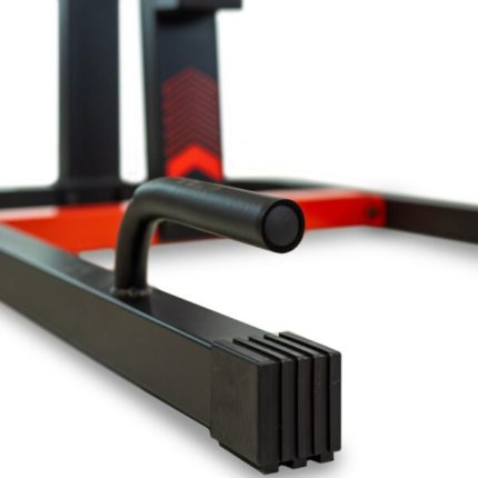 Close-up of a black metal exercise machine frame with a rounded grip bar and stacked rectangular pads; red accents are in the background.