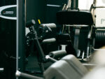 Leg-extension and leg-curl gym machine with black padding and yellow handle lever inside a workout area.