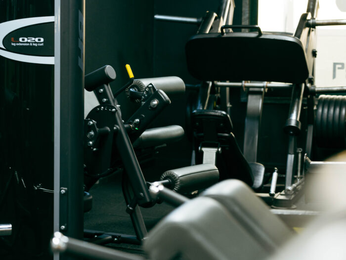 Leg-extension and leg-curl gym machine with black padding and yellow handle lever inside a workout area.