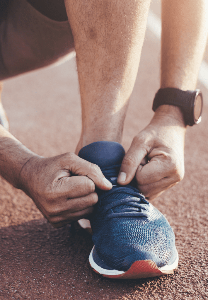 Person tying the laces of a blue running shoe on a track, wearing a wristwatch.