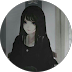 Portrait of a person with long dark hair and bangs, wearing black clothing, looking at the camera in a dimly lit setting.