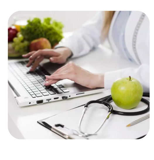 Healthcare professional typing on a laptop at a desk, with a stethoscope and a green apple nearby.