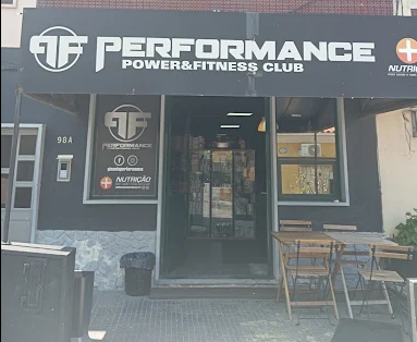 Storefront of Performance Power & Fitness Club with logo, glass door entrance, and outdoor seating.