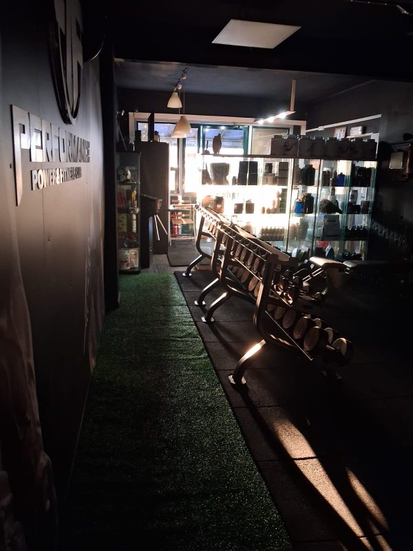 Dimly lit gym or fitness studio with a row of exercise machines and a glass display cabinet in the back.