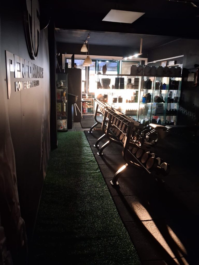 Dimly lit gym or fitness studio with a row of exercise machines and a glass display cabinet in the back.