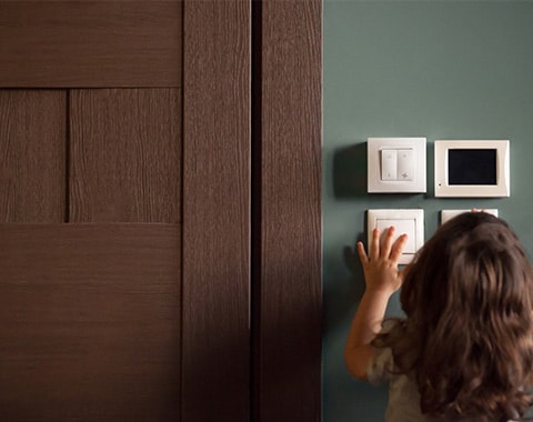 Child reaching toward wall switches and panels beside a dark wood door in a home interior
