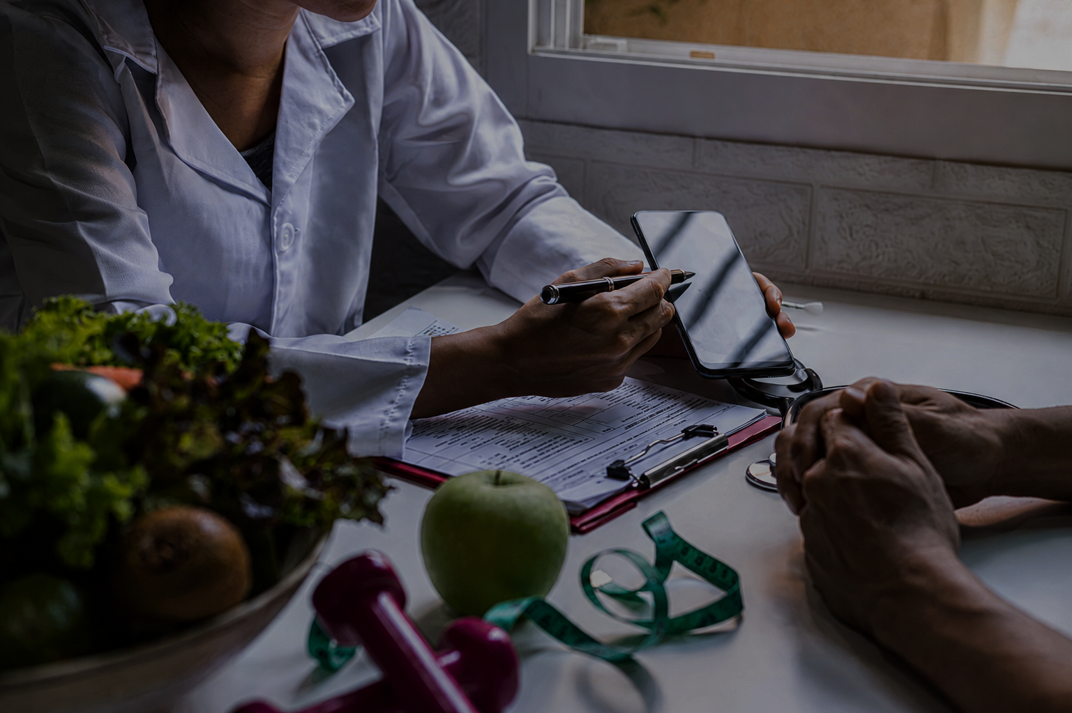 Healthcare professional in a white coat takes notes with a stylus at a desk; smartphone, stethoscope, measuring tape, and fresh produce nearby.