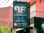 Sign advertising 'Performance Power & Fitness Club' with circular logo, social icons, and nutrition text on a storefront.